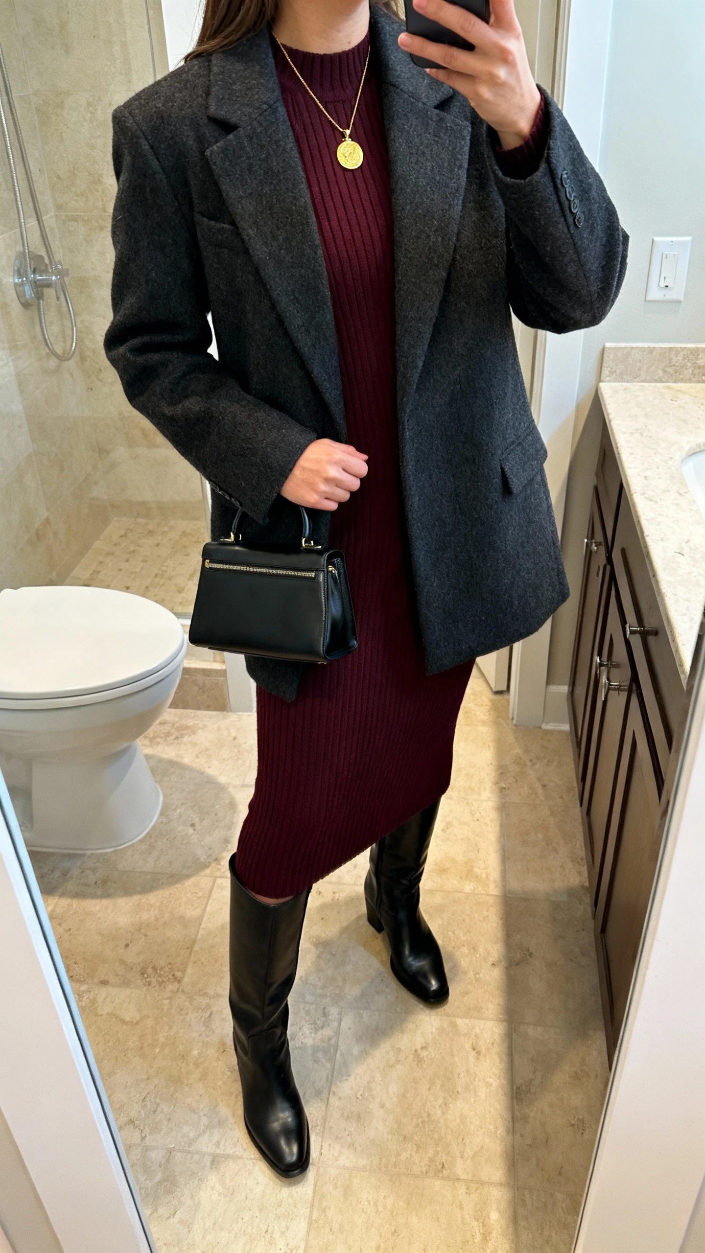 iPhone mirror selfie of a woman in a luxe ribbed knit midi dress in deep burgundy, black knee-high leather boots, a tailored wool coat in charcoal, gold pendant necklace, black structured top-handle bag, face not visible, side angle, bathroom full-length mirror, warm indoor lighting, iPhone photo quality.